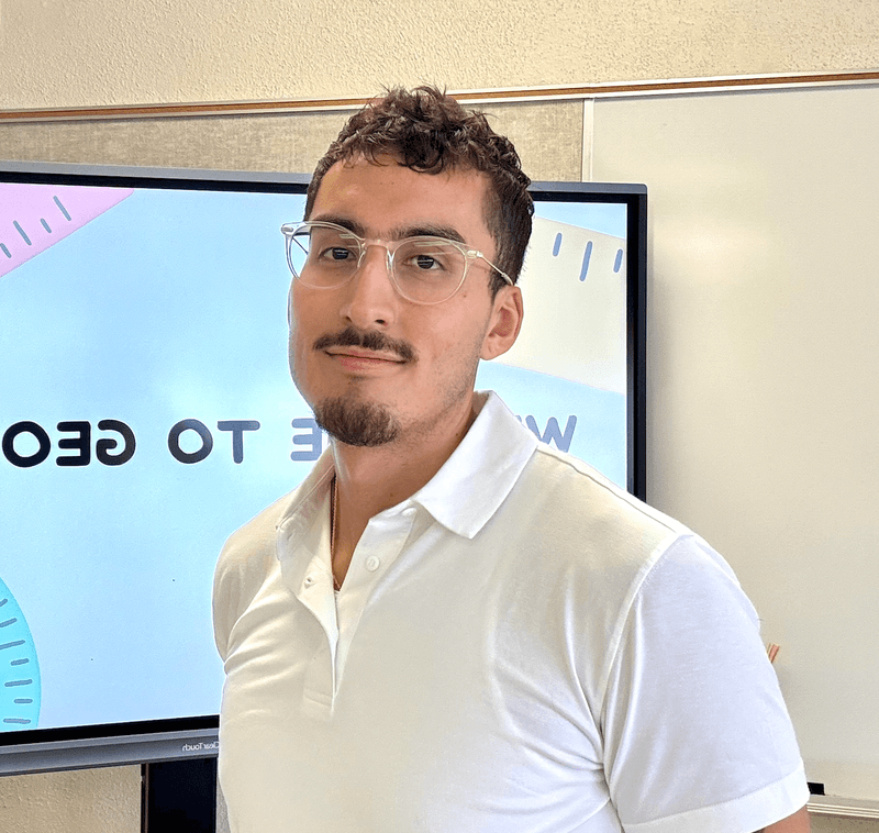 Juan Oviedo, founder of UnpackMath, standing in his classroom in front of a whiteboard